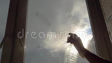 家庭主妇在窗户玻璃清洁剂上喷洒清洁剂并用刷子清洗